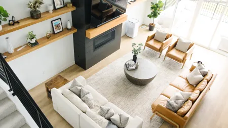 Bright modern living room with tan leather sofa, white couch, armchairs, round coffee table, and fireplace.