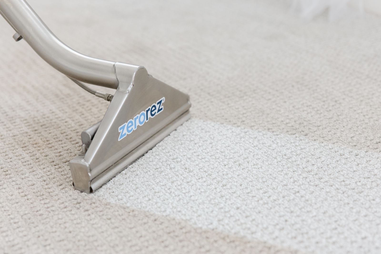 Close up on the front of a Zerorez Zr Wand cleaning a white textured carpet and leaving a clean stripe