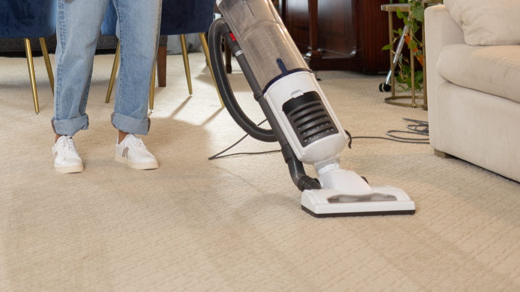 white upright vacuum being used to clean before carpet cleaning by a person wearing white tennis shoes